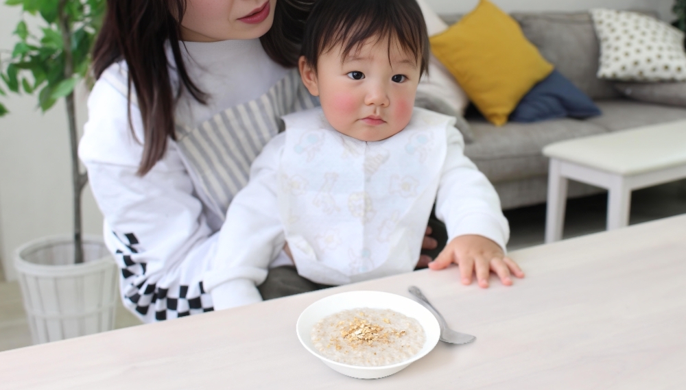 お母さんに抱えられた赤ちゃんの前の机の上に離乳食がある様子